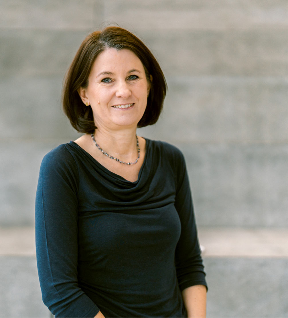 Auf dem Bild  ist Hebamme  Christine Lerzer zu sehen. Sie hat mittellange braune Haare, blaue Augen, trägt ein dunkelblaues langärmliges Shirt dazu eine Kette. Sie lächelt sympatisch und freundlich in die Kamera.